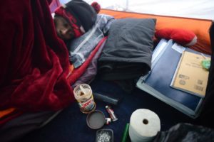 Gerri Jackson, 22, going back to bed next to his school books after scraping the bottom of a Skippy peanut butter and chocolate jar for his breakfast on a cold early Sunday morning in his tent in a wooded area of a Santa Rosa park. November 24, 2013. (Photo: Erik Castro/for The Press Democrat)