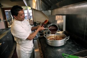 Mateo Granados pours mole sauce on lamb meat that will go into enchiladas.