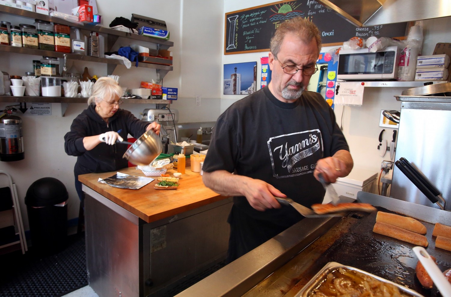 John Vrattos cooks a sausage on the grill as his wife Francesca prepares Greek fries at their Penngrove restaurant, Yanni's Sausage Grill. They have been married for 35 years. (Christopher Chung / The Press Democrat) 