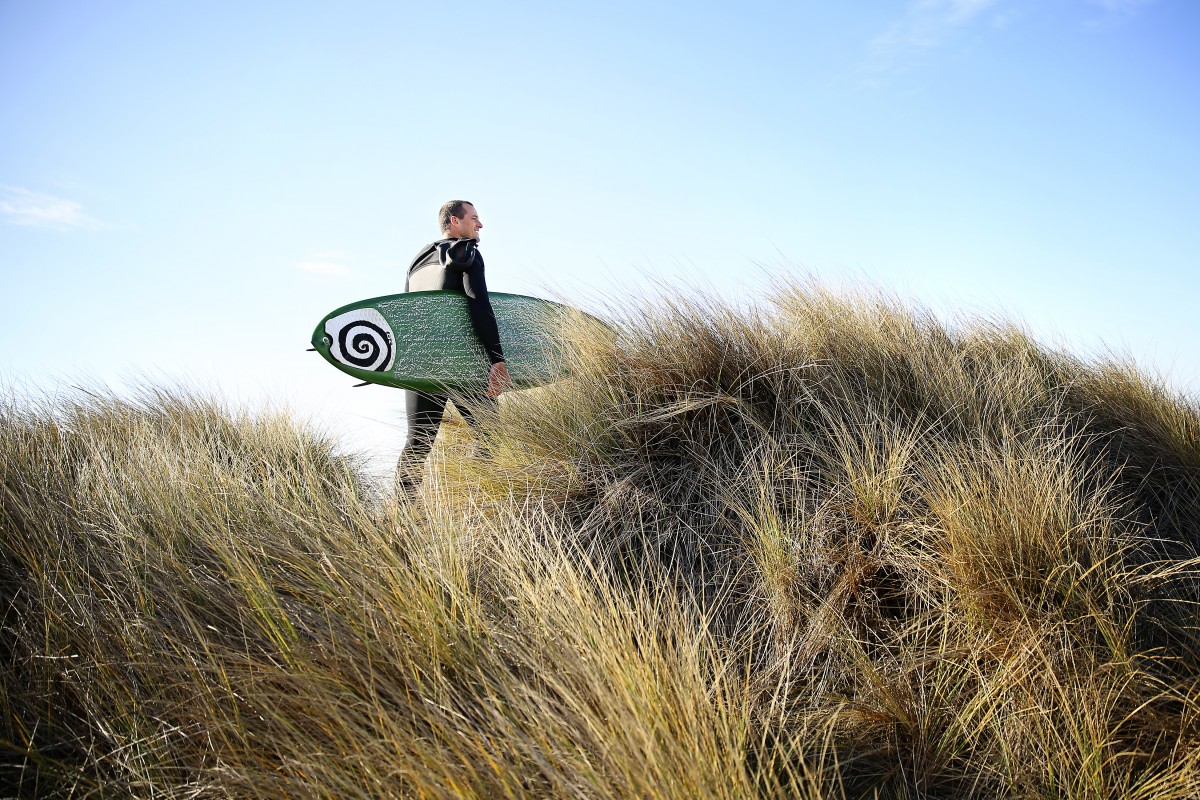 Nate Buck walks through the sand dunes by his home in Salmon Creek to go out for a surf session. (Photo by Conner Jay)