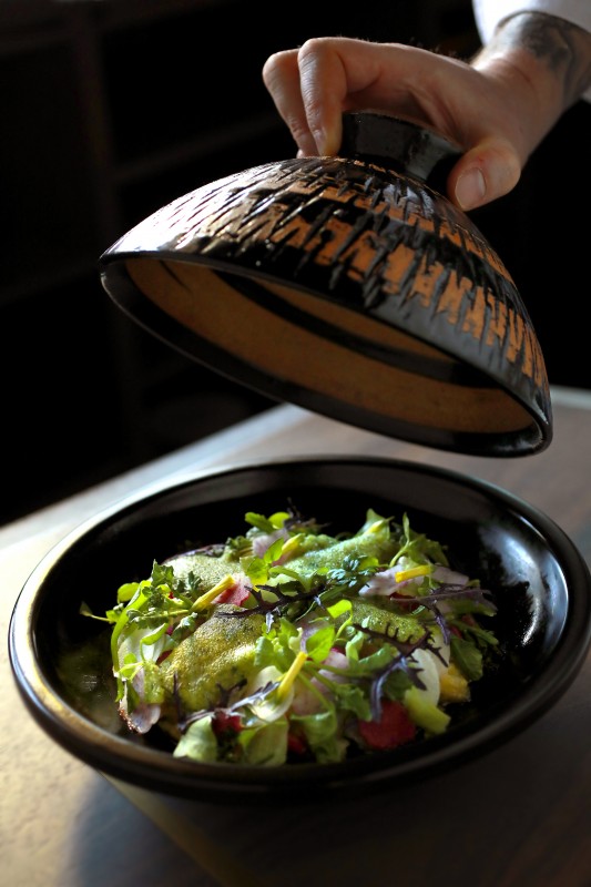 A dish called "Tilefish, Blue Foot," and Chnterelle "Fukkura-San" with Leeks, Brassicas from the Farm, Sansho, and Chamomile Dashi Borth is first presented at the table in the Kapanese donable it was cooked in, then whisked away to be played for serving