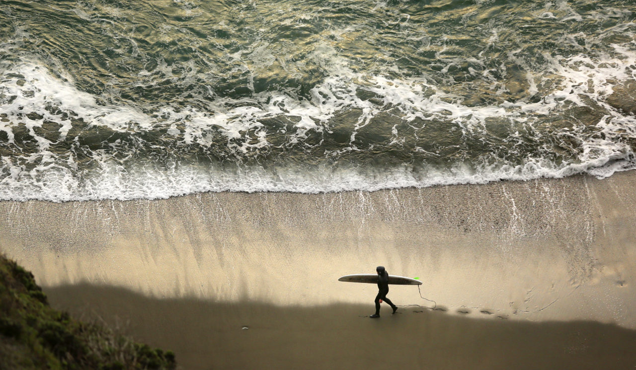 Eric Austensen walks along Goat Rock State Beach looking for waves to surf. (Photo by Conner Jay)