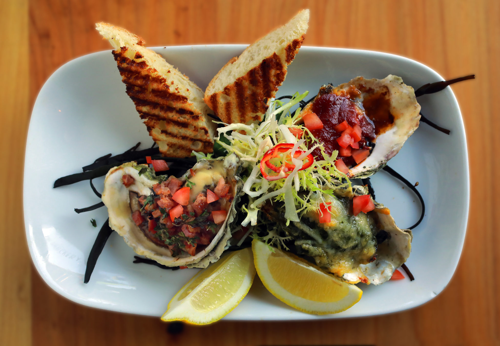 From left, Tasso Herb Grilled Oyster with cure ham and herb butter, Rockefeller Grilled Oyster with spinach, parmesan, Pernod, and garlic, Classic Chipotle BBQ Oyster all served with lemon and grilled baguette from The Shuckery in Petaluma. (John Burgess/The Press Democrat)