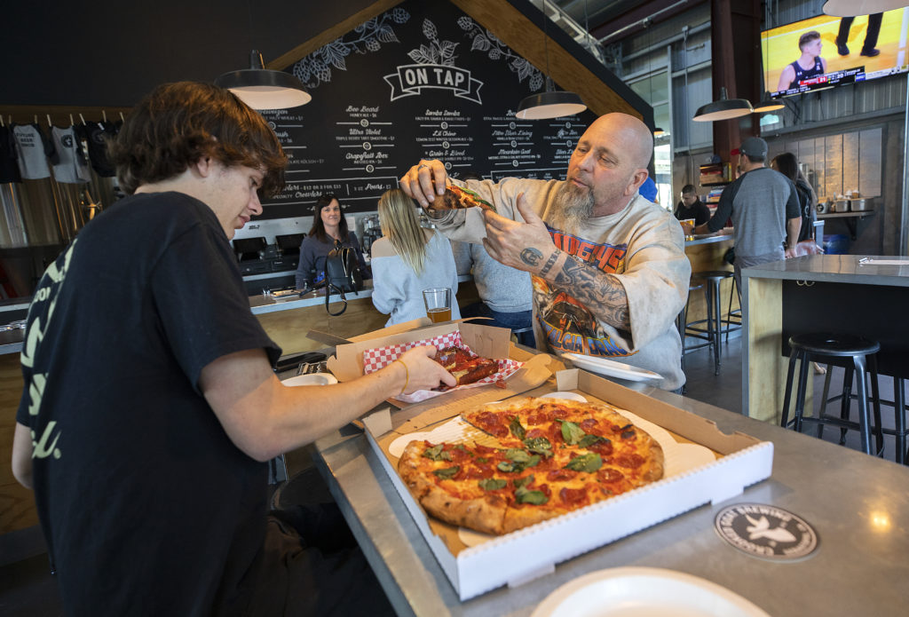Jesse, left, and Geo Borba dig into some Acre Pizza they ordered while having beers at Crooked Goat in Sebastopol's Barlow district. (John Burgess/The Press Democrat)