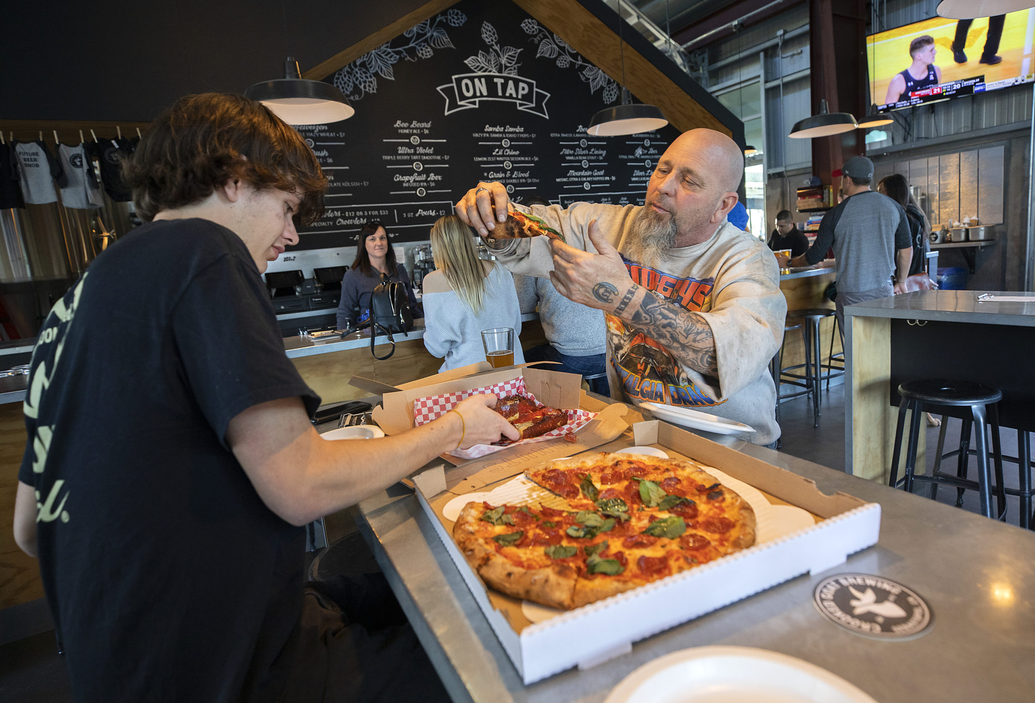 Jesse, left, and Geo Borba dig into some Acre Pizza they ordered while having beers at Crooked Goat in Sebastopol's Barlow district. (John Burgess / The Press Democrat)