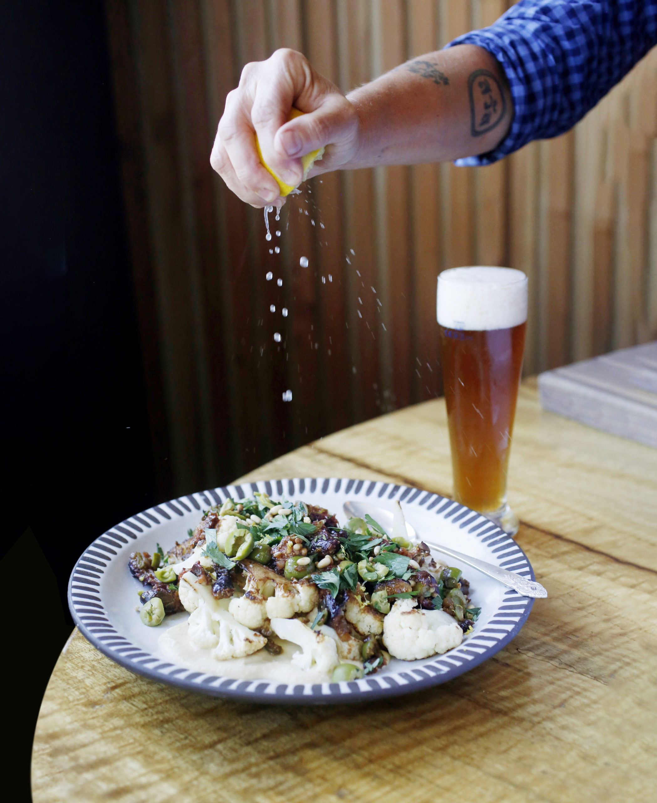 Chef Crista Luedtke squeezes a lemon on a plate of roasted cauliflower, pureed chickpeas, and topped with roasted figs, chopped green olives, pine nuts, and parsley at her restaurant Brot in Guerneville, Calif., on Wednesday, July 7, 2021.(Beth Schlanker/The Press Democrat)
