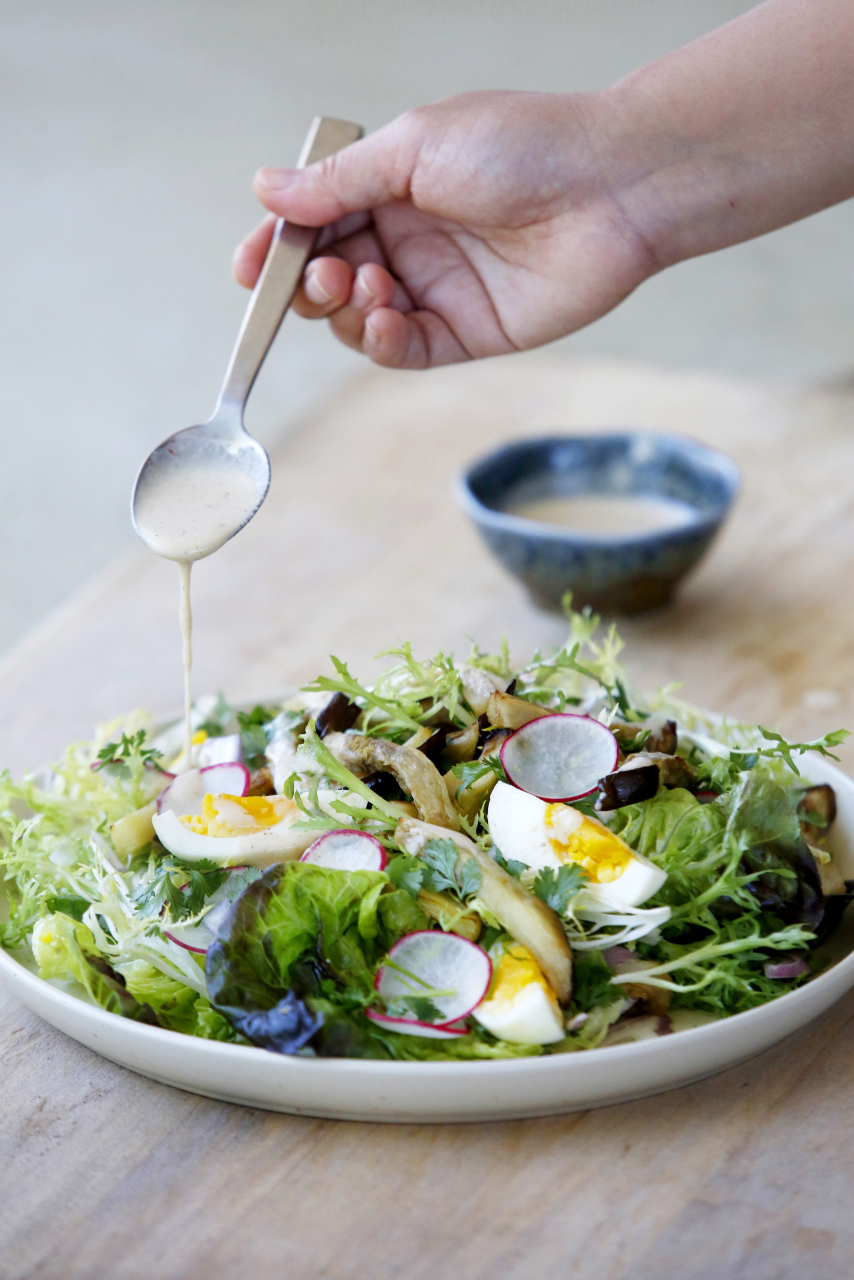 Chef Ploypailin Sakornsin drizzles a a chile-jam coconut milk dressing onto a salad of baked eggplant, soft boiled eggs, radishes, and shallots, atop a bed of little gem and frisee greens in Healdsburg, Calif., on Tuesday, July 6, 2021.(Beth Schlanker/The Press Democrat)