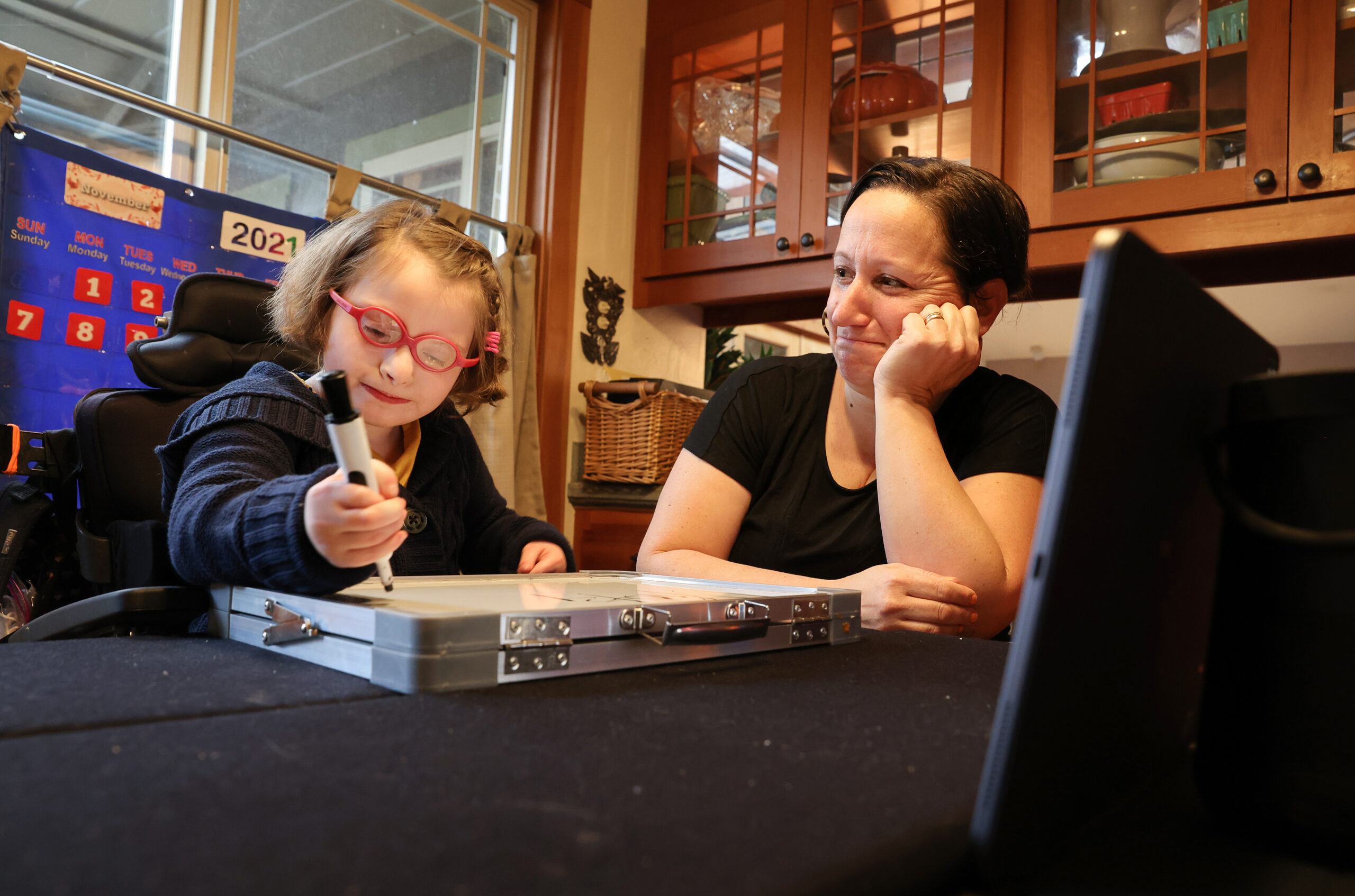 Andrea Loveday-Brown watches her daughter, April, 8, write on a white board during her online special day class in the West County Consortium at home in Sebastopol on Wednesday, November 10, 2021. (Christopher Chung/ The Press Democrat)