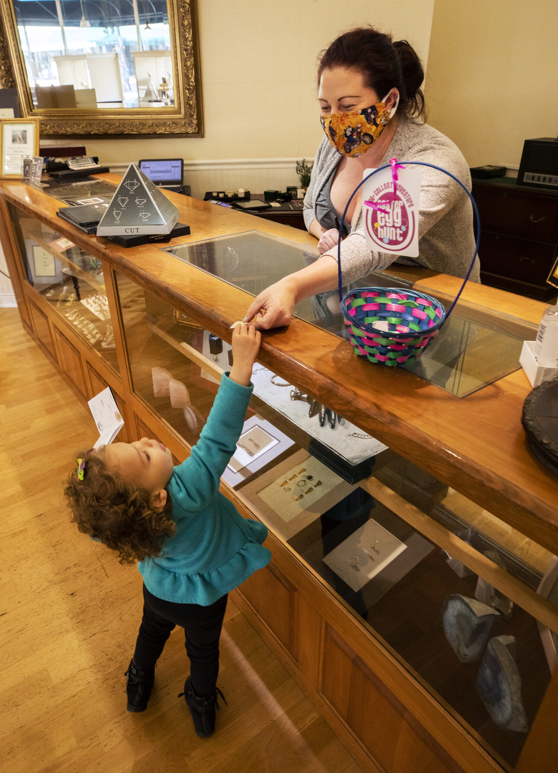 Jennifer Reynolds hands out a treasure hunt sticker to Talitha Blair, 3, at Timothy Patrick Jewlers in downtown Santa Rosa on Tuesday, March 16, 2021. Downtown Santa Rosa businesses are hoping to drum up some business with an Easter "Egg" Hunt where kids can collect stickers from businesses and turn them in for prizes. (Photo by John Burgess/The Press Democrat)