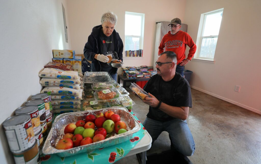 June Michaels, left, founder of Food Runners, brings food to the Veterans Village in Santa Rosa, where tenants Rob Holley and Michael Kinney help unpack the delivery on Wednesday, Nov. 13, 2019. (Christopher Chung/ The Press Democrat)