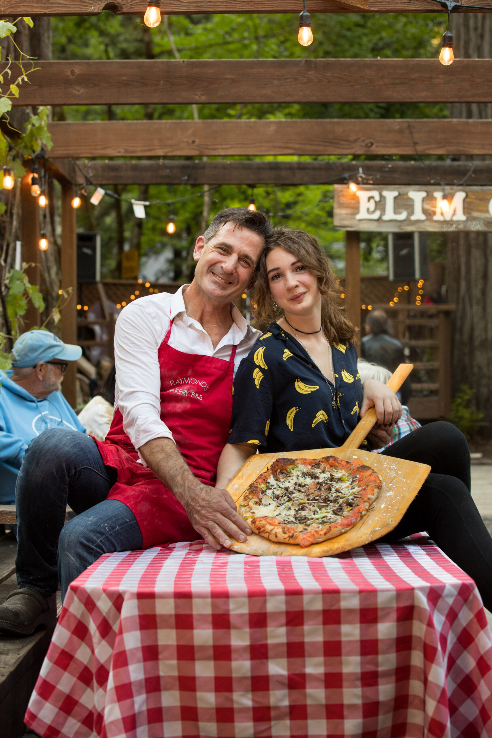Owner, Mark Weiss, and his daughter who works at the bakery, Ella Weiss, 17, hold one of their pizzas, during community pizza night with live music at Raymond's Bakery, in Cazadero, Calif., on Friday, May 13, 2022. (Photo by Darryl Bush / For The Press Democrat)