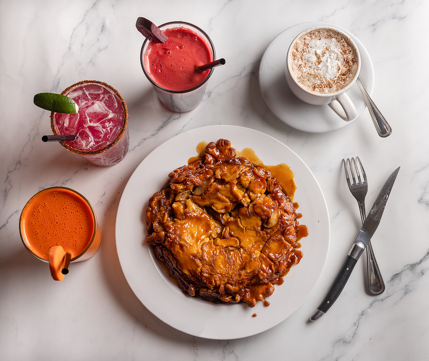 Dutch Baby, a German-style pancake with caramelized sugar, apples and a hint of nutmeg surrounded by, from left, the Sunshine with carrot, orange, ginger and turmeric; Prickly Pear Margarita; the Beet with carrot, celery, apple and ginger; and a Cafe Mocha on the menu at Brothers Cafe in Santa Rosa. Photo taken Thursday, April 27, 2023. (John Burgess / The Press Democrat)