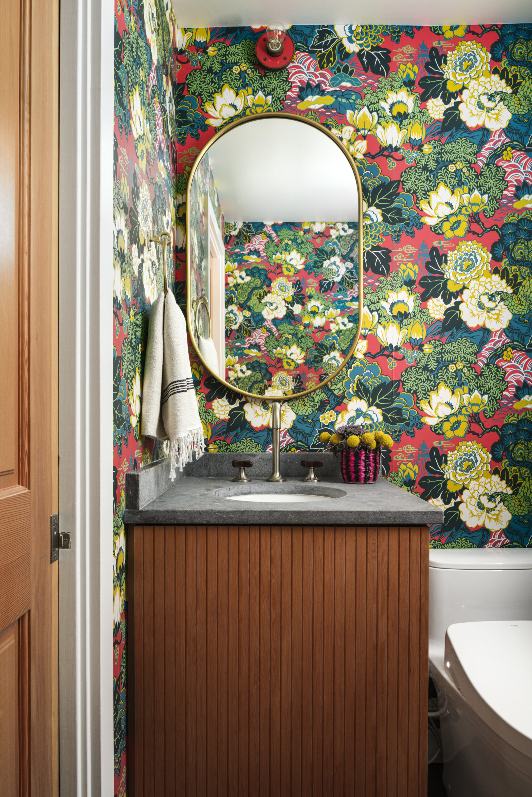 In the bathroom, heavily-patterned, color-saturated wallpaper is a wonderfully bold choice. Wood cabinets and a stone countertop anchor the look in a natural vein. (Christoper Stark)