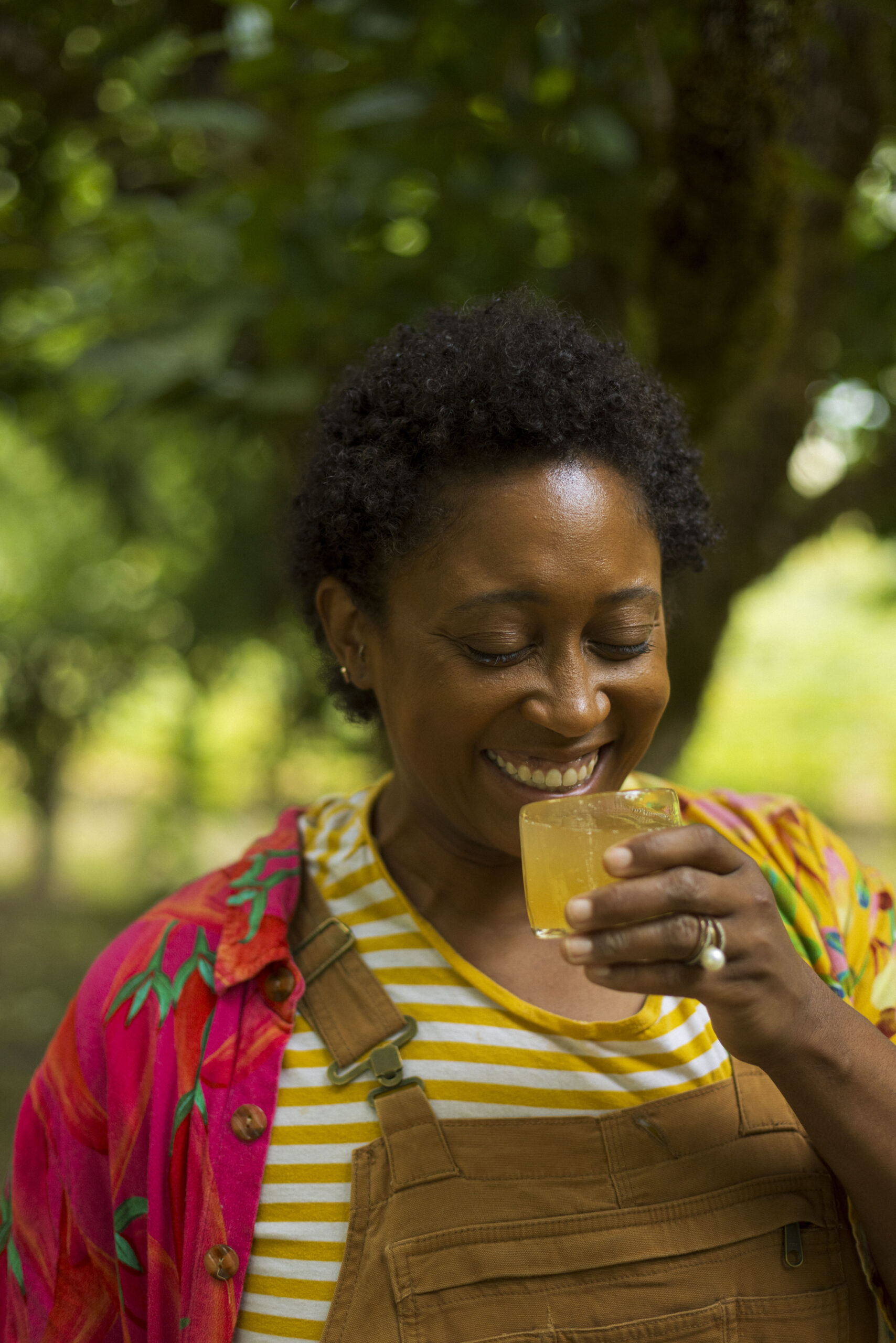 woman in a vibrant red shirt, striped shirt, and orange overalls sipping on some fermented beverages in Sonoma County