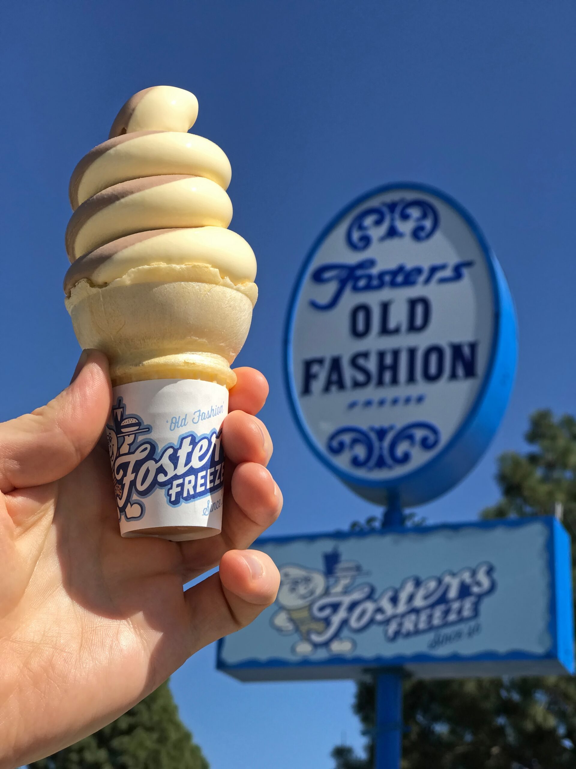 In front of a Fosters Freeze sign, a hand holds a vanilla and chocolate swirl ice cream cone. This restaurant chain was founded in 1946. (Kilmer Media/Shutterstock)