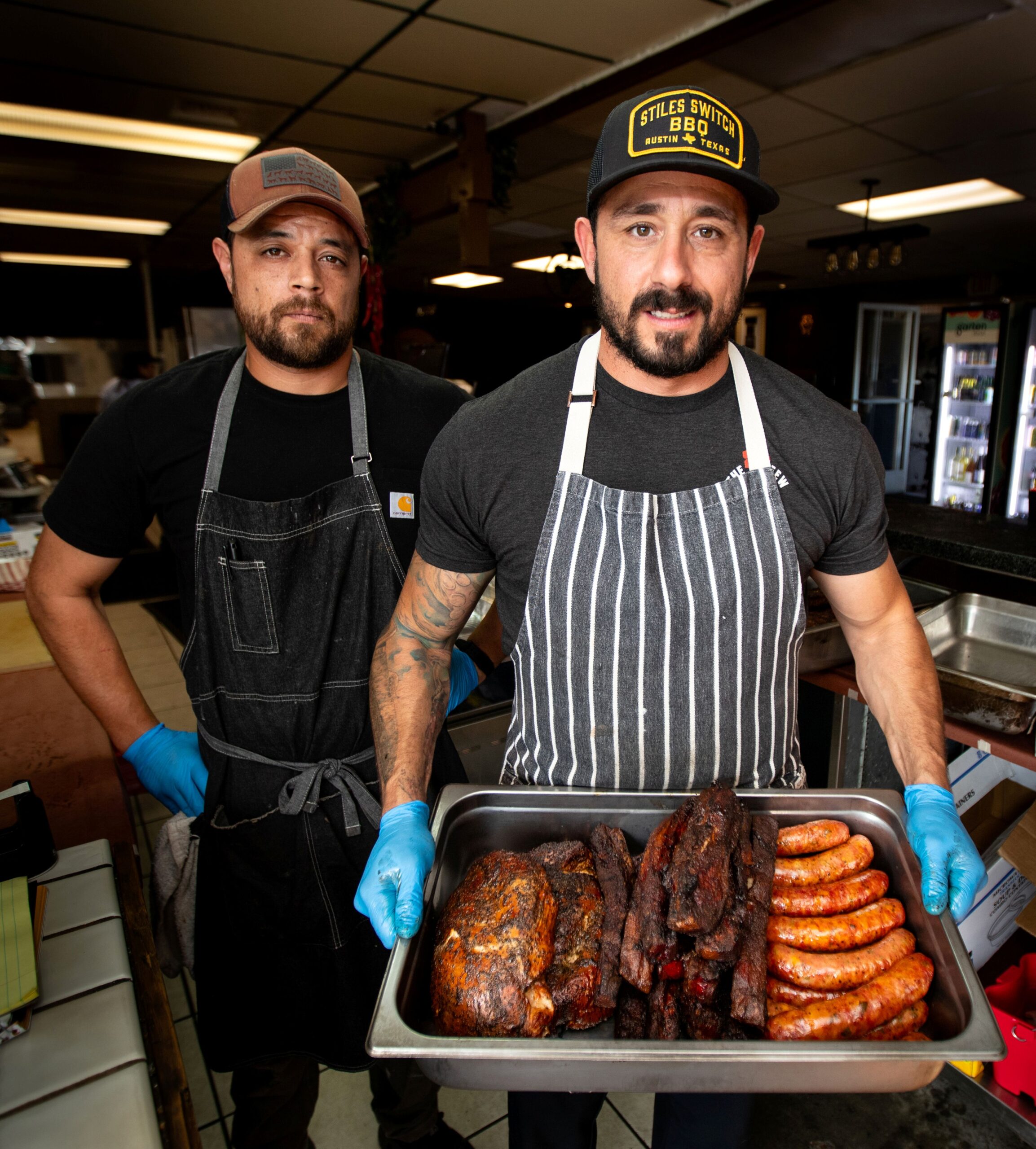 Red Eye Barbecue owner Bob Costarella holding pan of barbecued meats alongside sous chef Brendon Welcker