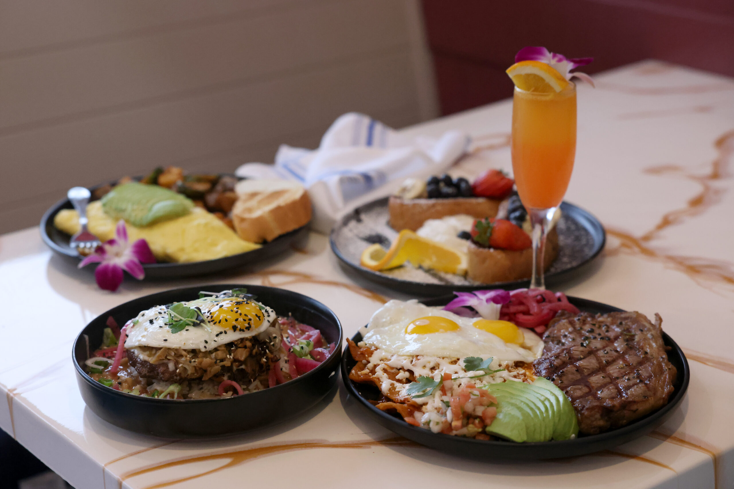A variety of dishes including Loco Moco, counterclockwise from left, chilaquiles with steak and eggs, French toast, an Americano omelette, and a classic mimosa at Bubbles and Delights Cafe in Petaluma Sunday, Dec. 21, 2025. (Beth Schlanker / The Press Democrat)