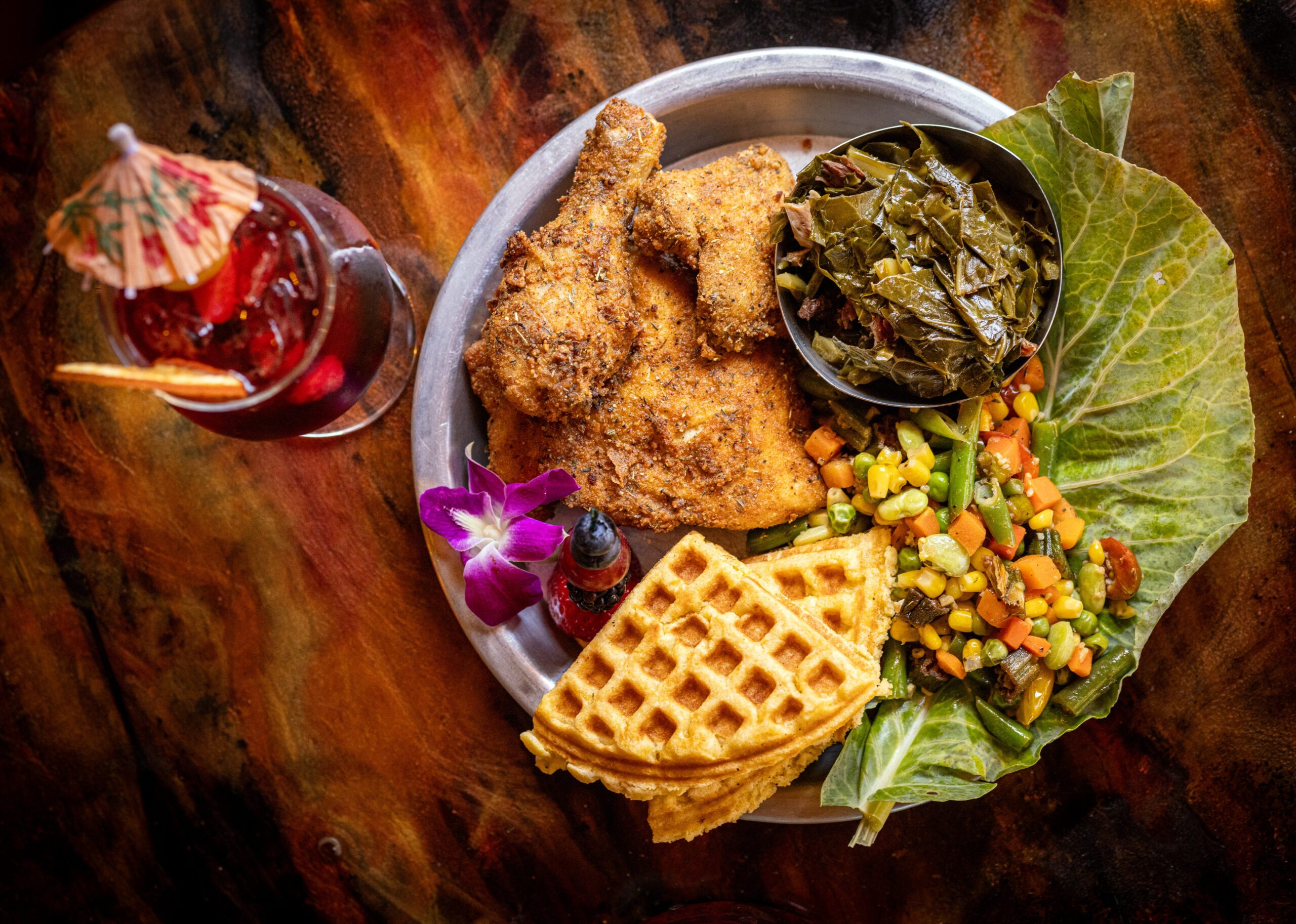 Buttermilk Fried Chicken with collard greens, succotash, cornbread waffle and crack butter with a Hibiscus Flower N/A cocktail from Saucy Mama’s Jook Joint Friday, July 18, 2026 in Guerneville. (John Burgess/The Press Democrat)