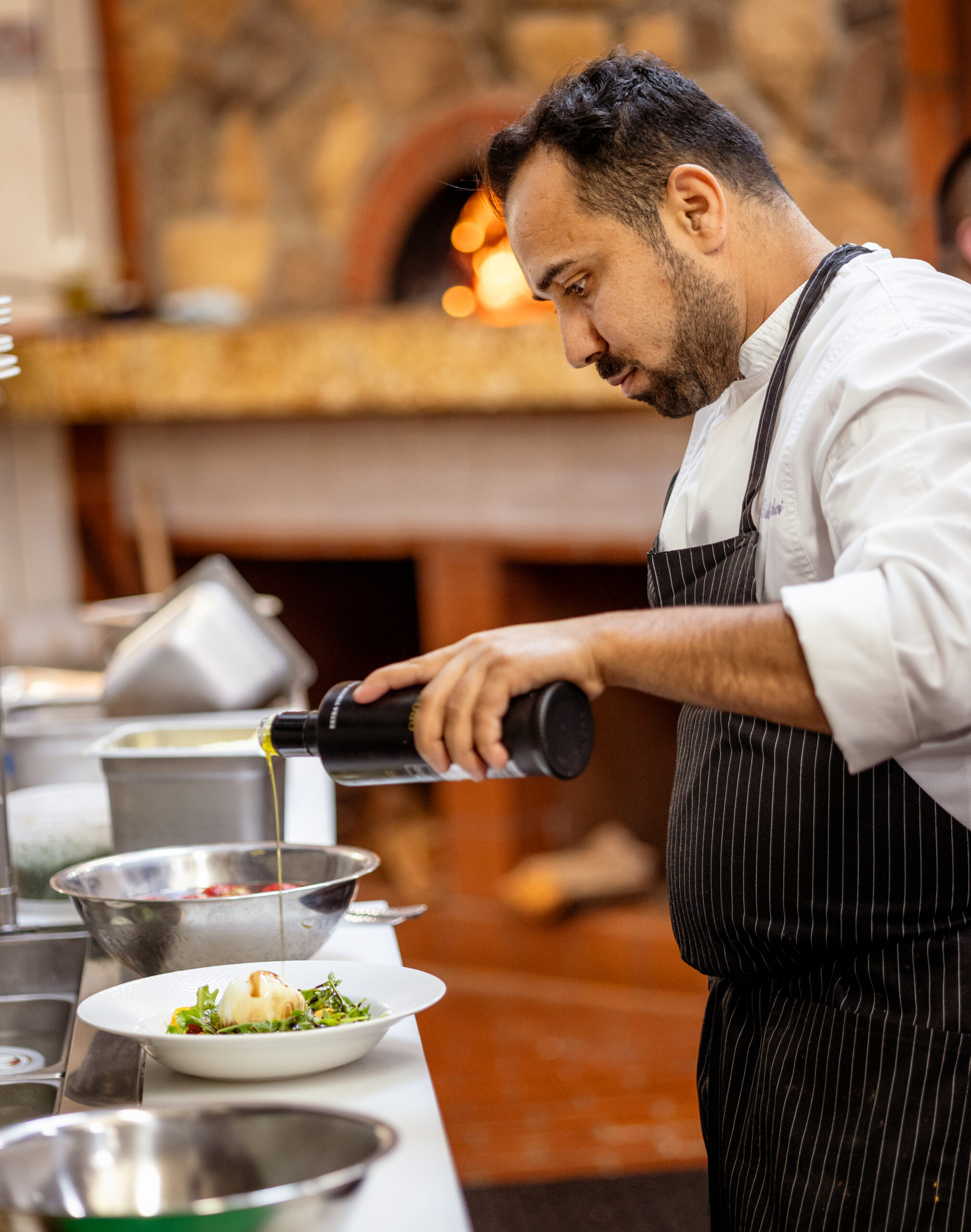 Owner/chef Baki Bekci finishes a burrata salad with olive oil in the kitchen at Capriciano Osteria